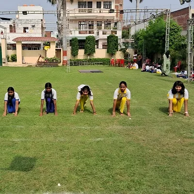 Five girls in sports uniform crouched in a starting position on a grassy field, ready for a race during a school sports event