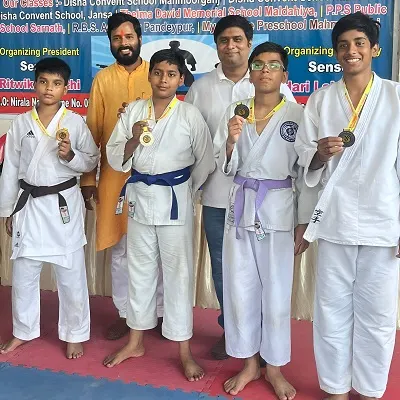 Four boys in karate uniforms proudly displaying medals with two adults standing behind them at a martial arts event