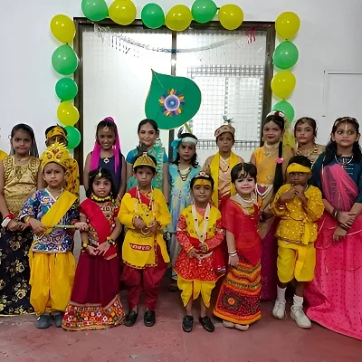 Group of children dressed in colorful traditional attire for a cultural celebration, standing under a green and yellow balloon arch